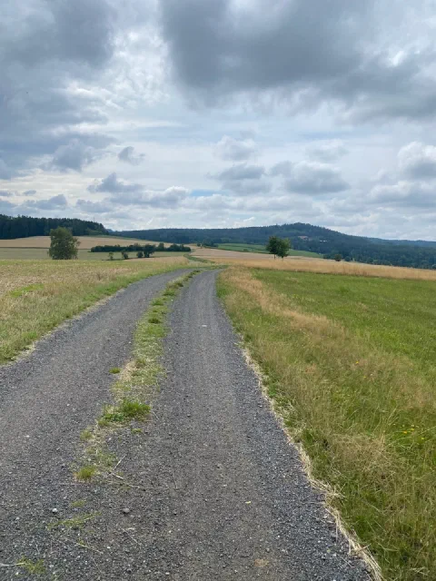 Empty gravel track towards hills under a grey-blue sky