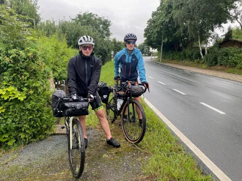 Both riders in rain jackets with their loaded bikes on a wet roadside