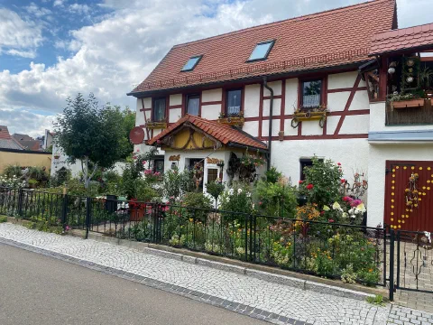 Half-timbered house with a red roof behind an iron fence and a flower garden