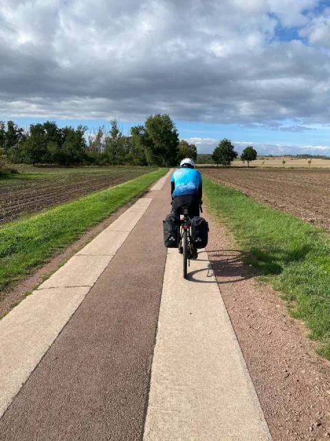 Rider in a blue jersey on a concrete-slab cycle track between fields under a big sky