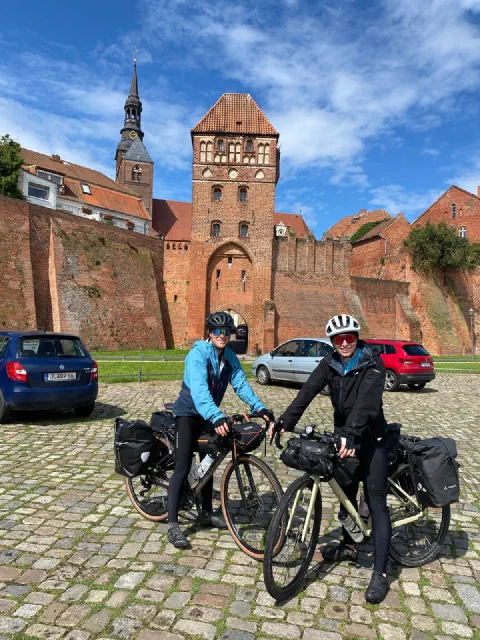 Both riders with loaded bikes in front of Tangermünde's brick city gate on cobblestones