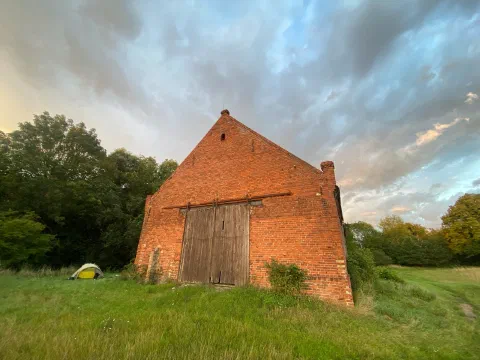 Brick barn gable against evening clouds, a yellow tent beside it