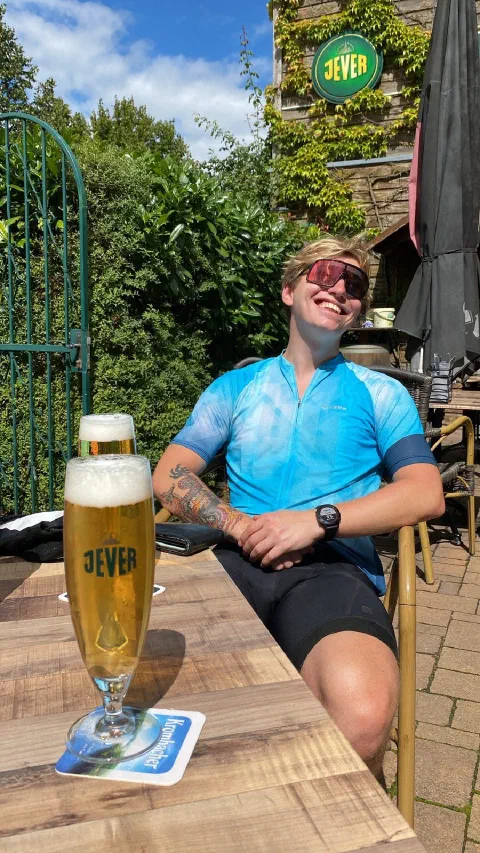 Rider in sunglasses with a Jever beer in a sunny beer garden, smiling
