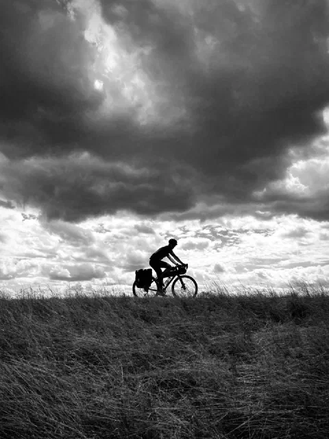Black-and-white silhouette of a rider on a grassy ridge under heavy clouds