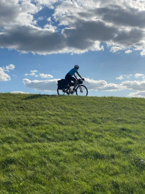 Rider on a green dike crest against big white clouds and a blue sky