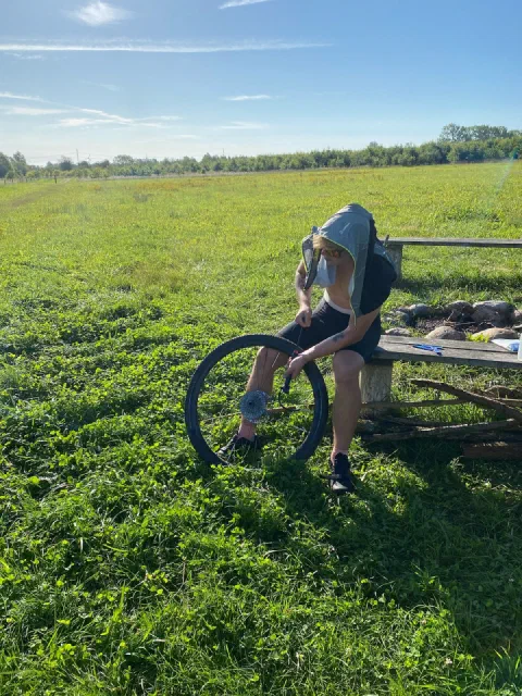 Puncture stop: a rider in a hoodie repairing a tyre on a bench in a meadow