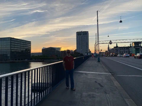 Friend at the railing of a Copenhagen bridge at sunset, skyline and street lamps