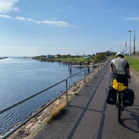 Rider on a path along a harbour inlet, sun on the water