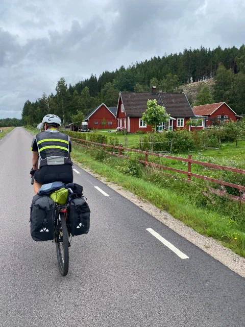 Rider on a cycle lane past red Swedish farmhouses and a rail fence