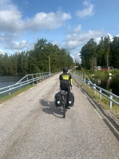 Rider in a neon vest on a causeway across a lake, red houses on the shore