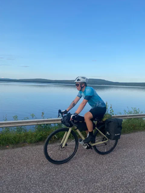 Rider in a light-blue jersey on a lakeside road in calm evening light