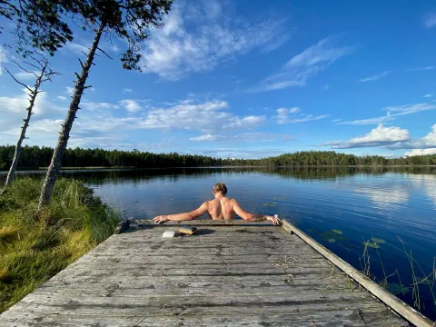Friend sitting at the end of a wooden jetty on a mirror-blue lake