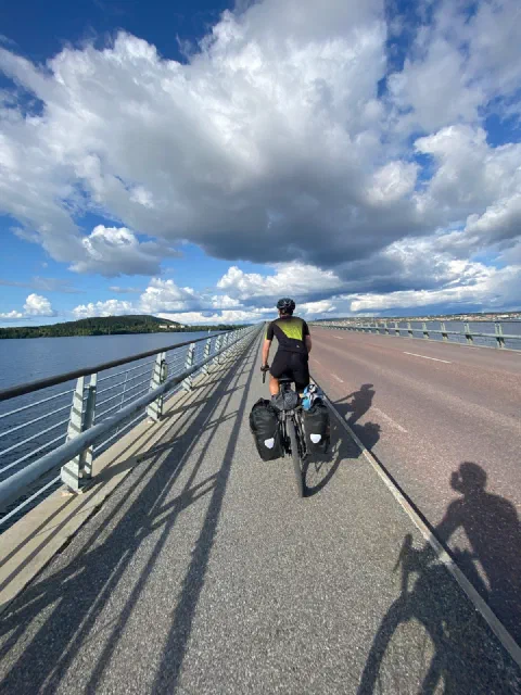 Rider on a long bridge over a lake, the railing's shadows on the road