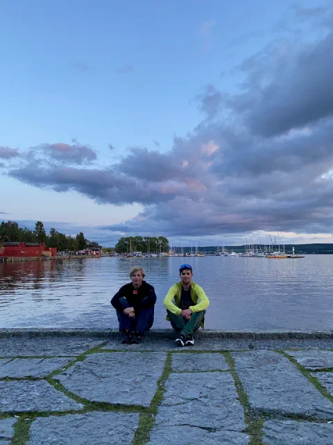 Both riders sitting on a stone quay by the lake under pink and purple clouds
