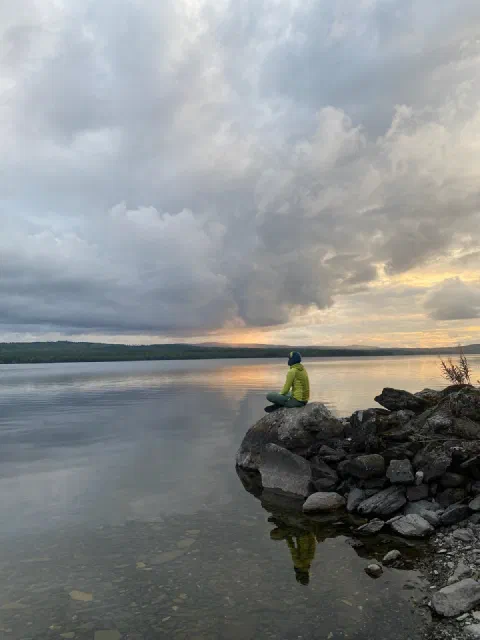 Friend sitting on a rock in the lake at sunset, mirrored in the water