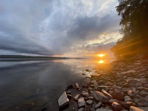 Dark stones on the shore, the sun sparkling on the lake and rays through the clouds