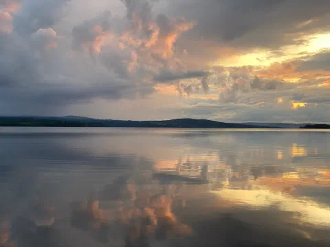 Pink and peach clouds after sunset, mirrored in a still lake
