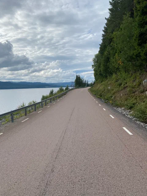 Empty rust-red road along a lake under a grey-blue sky