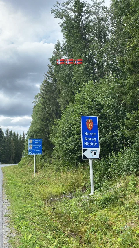 Blue border sign "Norge / Noreg / Nöörje" with flag stickers: the border to Norway