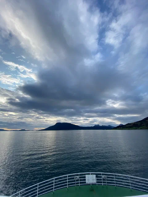 Ferry bow under a fan of clouds over the fjord