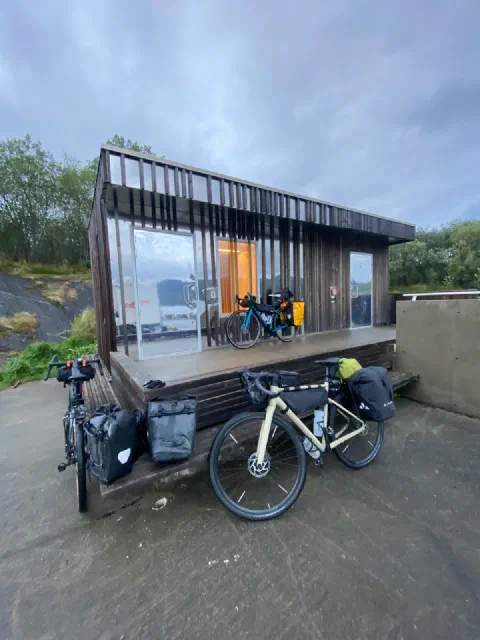 Glass-fronted wooden cabin with two bikes parked in front, in the rain