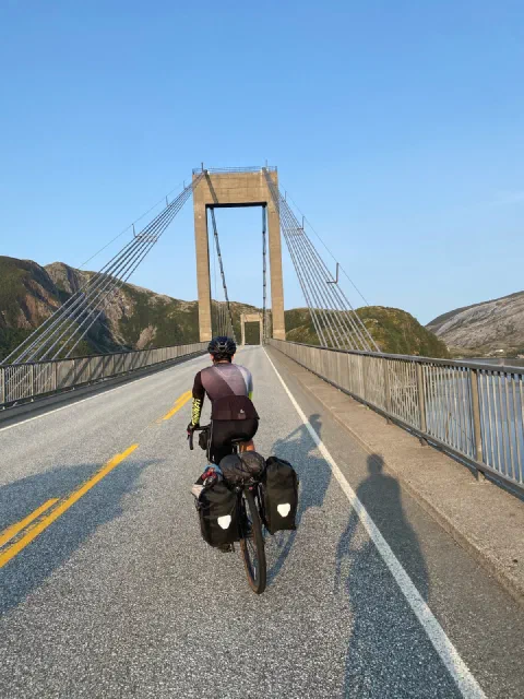 Rider crossing a suspension bridge in long shadows, the pylon above