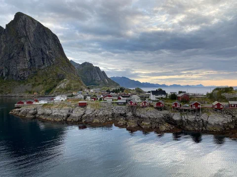 Hamnøy: a jagged peak above red fishing cabins on a rock spit, calm fjord