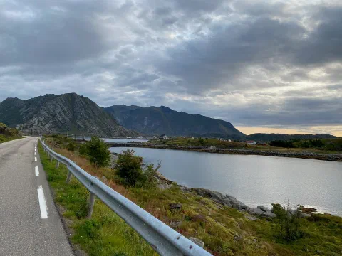 Road curving along the fjord, island mountains and a golden horizon
