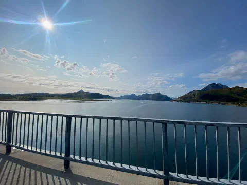 Calm fjord seen from a bridge, the sun a bright star in a blue sky