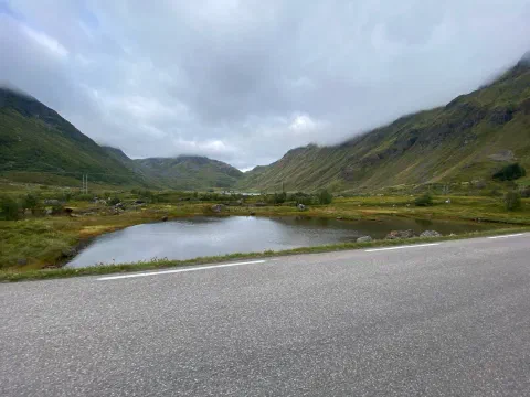 Misty U-shaped valley with a pond beside the road, low clouds on the peaks