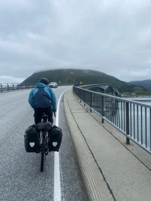 Rider in a blue jacket on a long bridge, a moody hill ahead