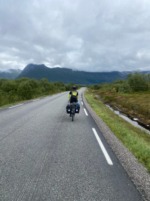 Rider on a straight road towards cloud-covered mountains