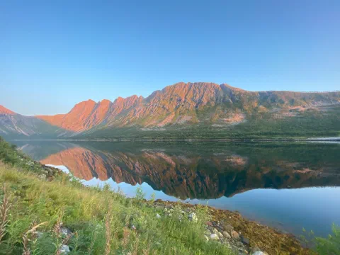 Pink-orange alpenglow on a mountain ridge, mirrored in the still fjord