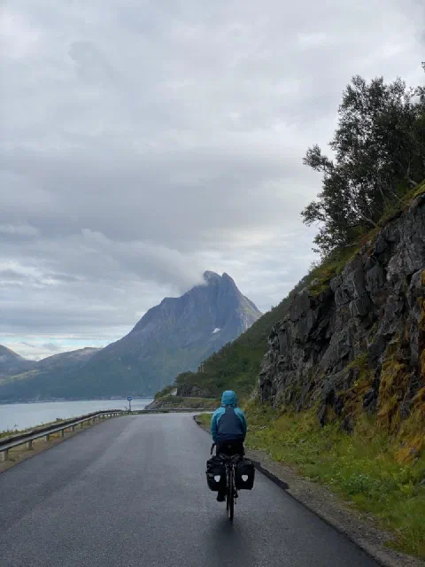 Rider in a blue rain jacket on a wet road beneath a pointed peak
