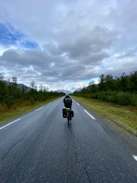 Rider in a neon vest on a wet road under towering clouds