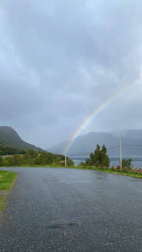 A rainbow over a wet road and the fjord, dark clouds